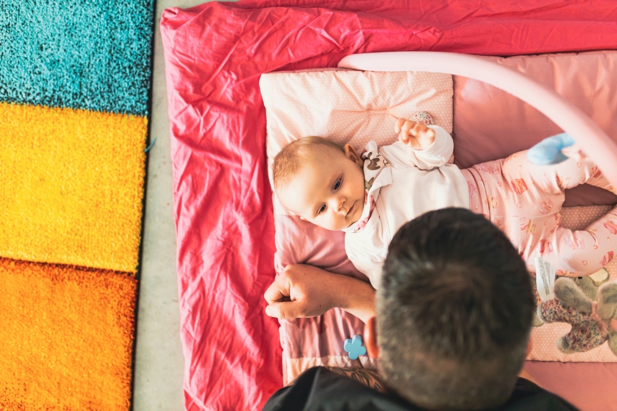 Säuglingt liegt auf bunter Krabbeldecke, Vater spielt mit diesem